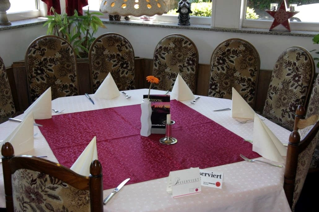 Großer gedeckter Tisch mit weißer Tischdecke, roter Mitteldecke, gefalteten Servietten und Reserviert-Schild